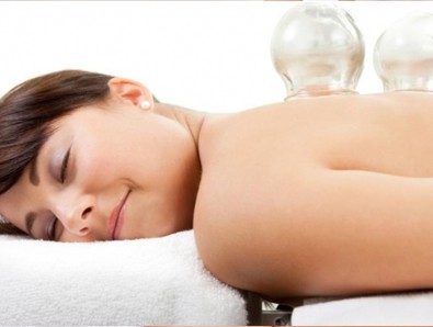 A woman lying on a massage table, savoring a glass of water to replenish her body's hydration after experiencing the blissful slipstream of massage cupping.